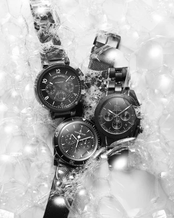 Three luxury wristwatches, Louis Vuitton and Dior brands, set against a backdrop of transparent spheres, creating a modern, monochrome still life.