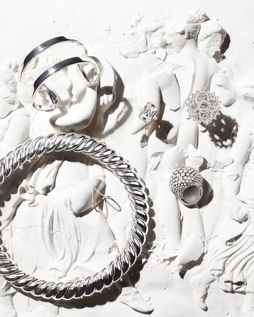 High-fashion jewelry pieces are displayed on a crumbling Greco-Roman-style sculpture, creating an elegant blend of vintage and modern design.