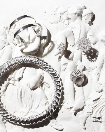 High-fashion jewelry pieces are displayed on a crumbling Greco-Roman-style sculpture, creating an elegant blend of vintage and modern design.