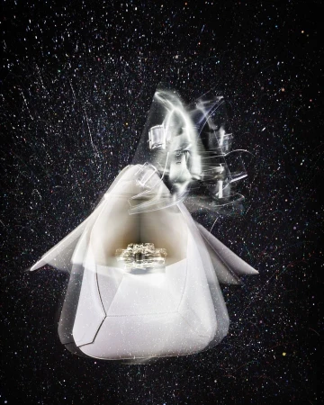 Abstract ring product shot with blurred edges, presented in a white paper package against a mottled black background.