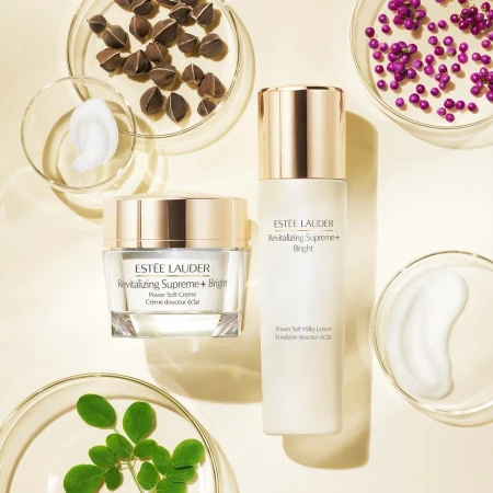 Two Estee Lauder Revitalizing Supreme+ Bright skincare products are displayed with petri dishes of botanical ingredients on beige.
