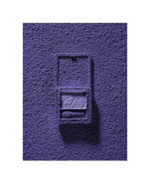 Eye shadow powder covers a purple makeup compact on a white surface, creating a monochromatic beauty still life.