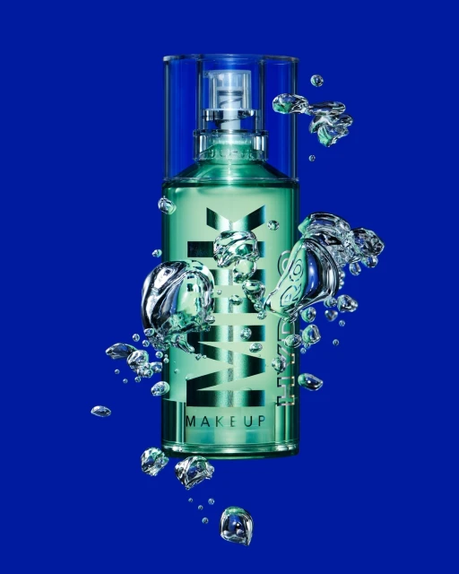 Turquoise MILK MAKEUP setting spray bottle with water droplets on cobalt blue background for beauty and cosmetics product shot.