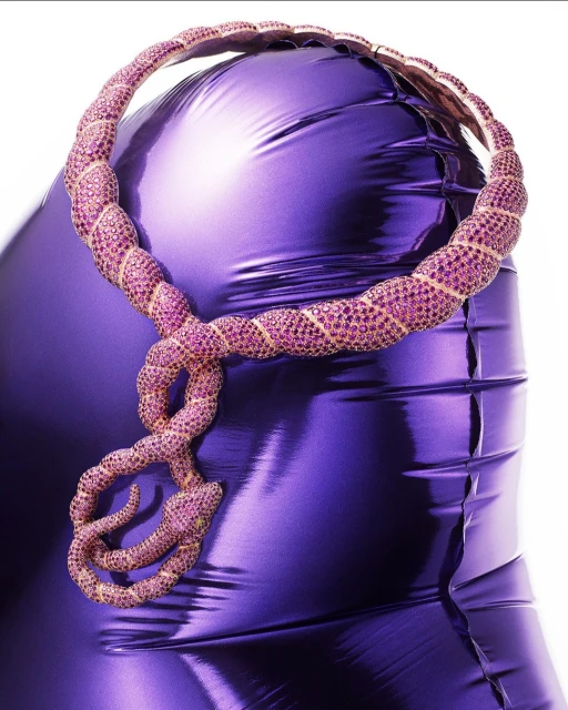 Shiny purple mannequin torso with a snake-shaped statement necklace made of pink and gold beads, against a white background.