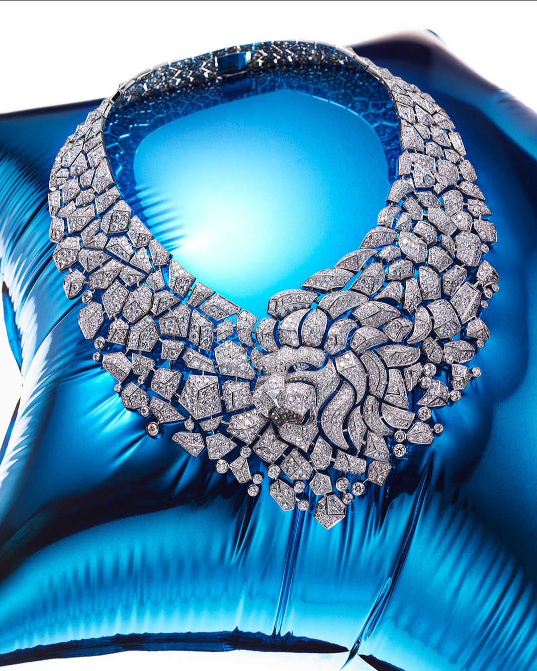 Statement necklace with a lion motif, featuring diamond embellishments on a shiny, vibrant blue surface, showcased in a studio shot.