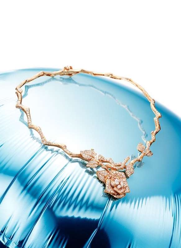 Elegant rose gold necklace featuring a rose floral pendant, adorned with sparkling accents, displayed on a glossy, reflective blue surface.