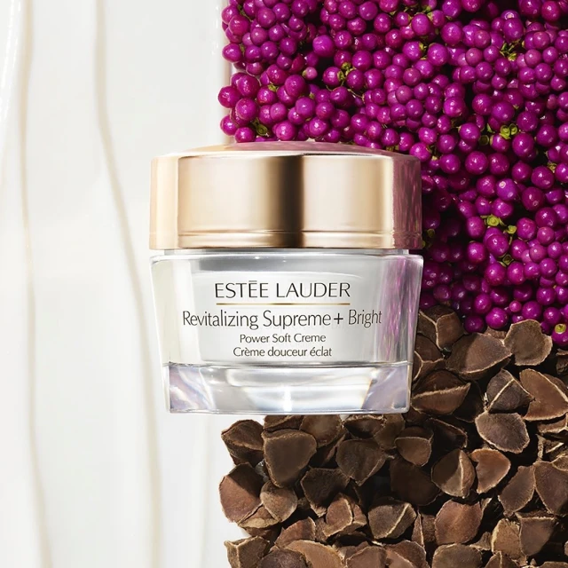 Close-up shot of Estee Lauder Revitalizing Supreme + Bright Power Soft Creme jar surrounded by pink berries and seeds on white surface.