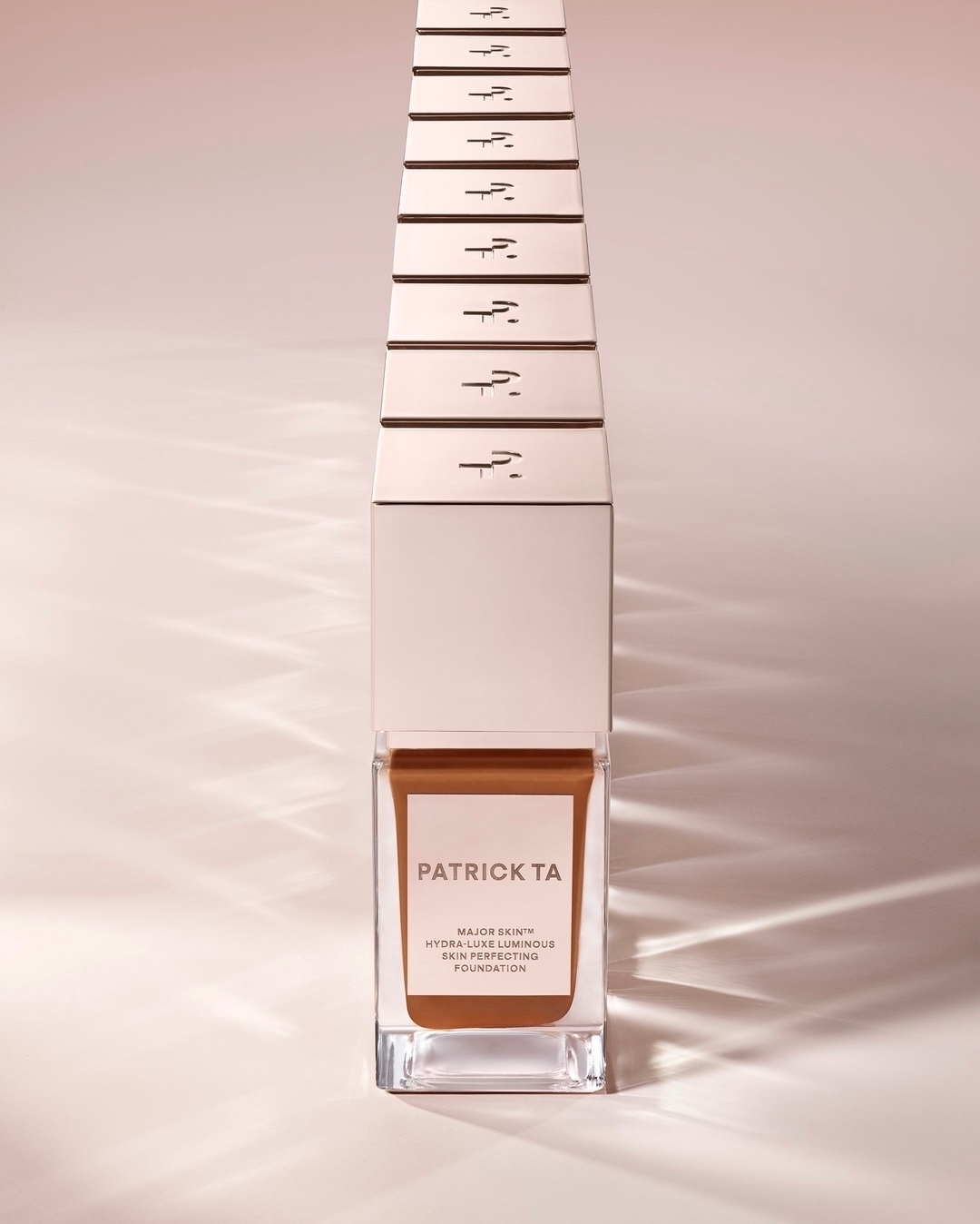 Patrick TA Major Skin Hydra-Luxe Luminous Skin Perfecting Foundation in clear glass packaging, studio shot on beige background.