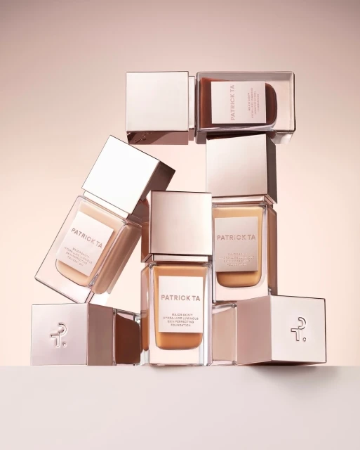 Stacked Patrick TA foundation bottles in a product shot with light peach background, emphasizing beauty, makeup, and luxury cosmetics appeal.