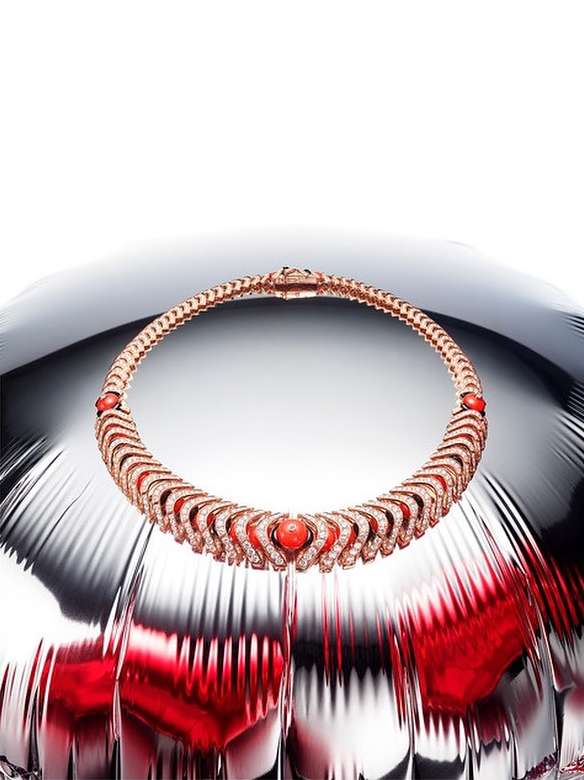 Elegant rose gold choker necklace with red coral accents displayed on a reflective silver metallic surface in a studio setting.