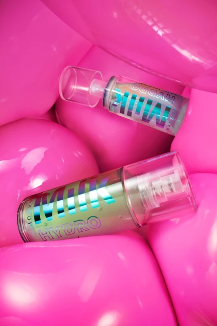 Two MILK MAKEUP HYDRO GRIP hydrating + smoothing primer tubes against a background of glossy, vibrant pink spheres.