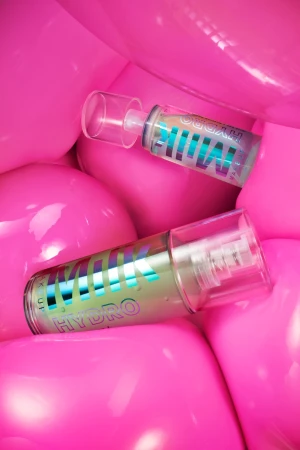 Two MILK MAKEUP HYDRO GRIP hydrating + smoothing primer tubes against a background of glossy, vibrant pink spheres.