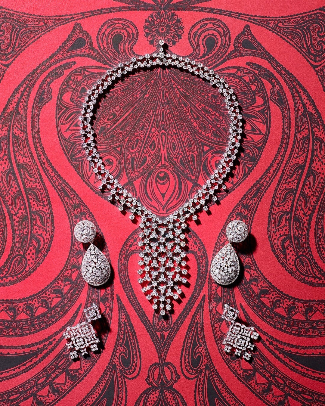Elegant diamond necklace with drop earrings and stud earrings showcased on a red patterned surface, emphasizing luxury and detail.