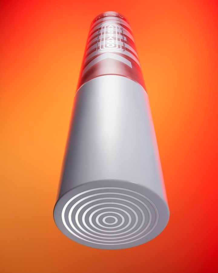 Elevated product shot of a gray, cylindrical container with concentric circles and geometric patterns against a gradient red and orange backdrop.