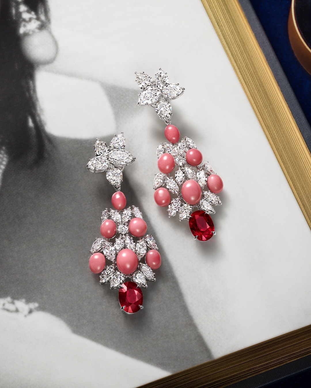 Elegant chandelier earrings with pink pearls, white diamonds, and red gems, displayed against a vintage portrait background.