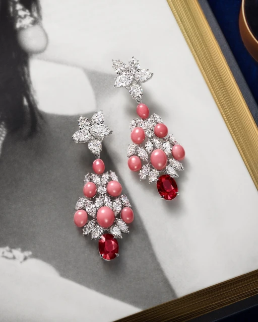 Elegant chandelier earrings with pink pearls, white diamonds, and red gems, displayed against a vintage portrait background.