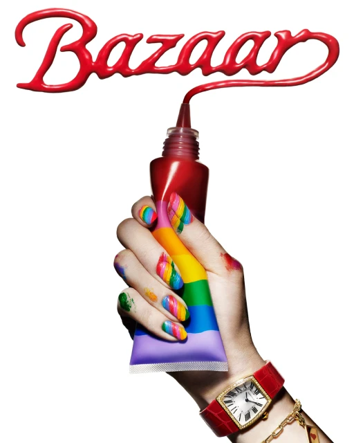 Close-up studio shot of a hand holding a paint tube, nails painted in rainbow colors, wearing a wristwatch, with red Bazaar text above.