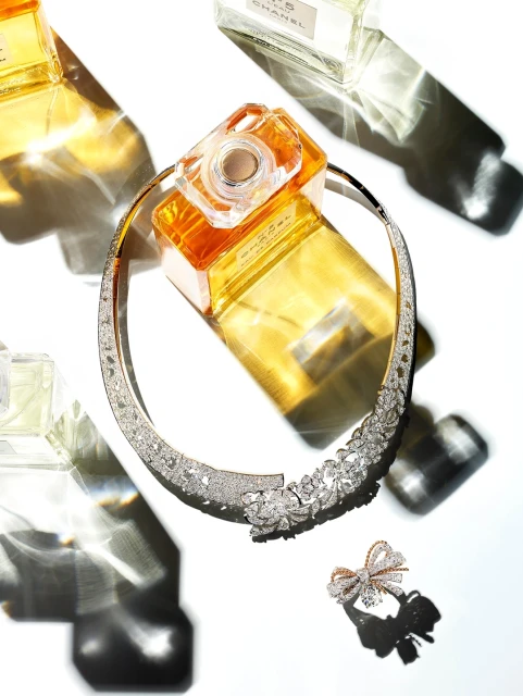 Still life of jewelry and Chanel perfume bottles in studio light featuring a crystal necklace, crystal bow, and glass perfume bottles.