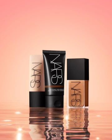 Three NARS foundation products in varying shades are displayed against a blurred coral background with a reflective surface. 