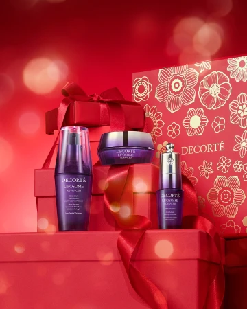 A collection of DECORTE skincare products are displayed on stacked red gift boxes, against a red backdrop, promoting beauty and skincare.