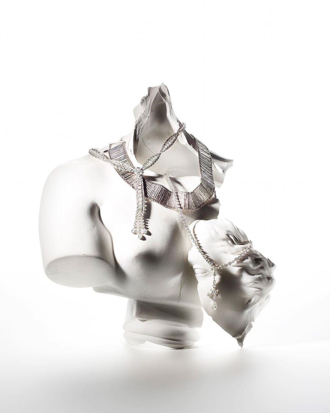 Necklace and bracelet draped on fragmented white plaster busts against a white background, jewelry product shot for beauty and fashion.