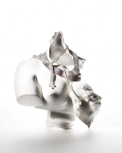 Necklace and bracelet draped on fragmented white plaster busts against a white background, jewelry product shot for beauty and fashion.