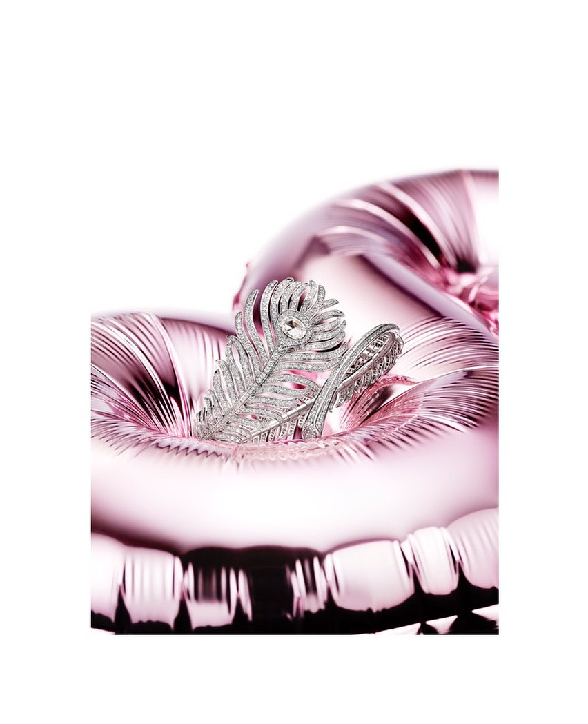 Close-up of a silver-toned metal feather-shaped ring with a stone setting, resting on a pink metallic heart-shaped balloon.