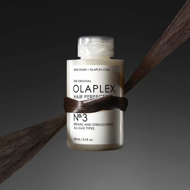 Olaplex No. 3 Hair Perfector bottle on a dark background with a strand of dark hair wrapped around the center of the bottle.