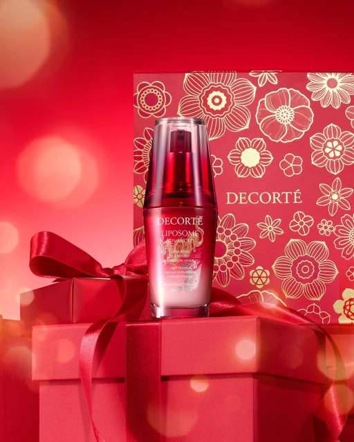 Decorté Liposome serum bottle atop stacked red gift boxes with floral patterned background, product shot for beauty and skincare promotion.