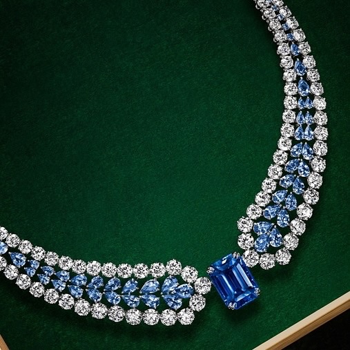 Elegant diamond necklace featuring blue gemstones set against a luxurious dark green backdrop, highlighting jewelry craftsmanship.