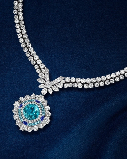 A luxurious diamond necklace with a large aquamarine pendant is set on a dark blue textured background in a close-up studio shot.
