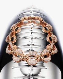 Close-up product photograph of a diamond-encrusted gold link necklace resting against a reflective metallic surface