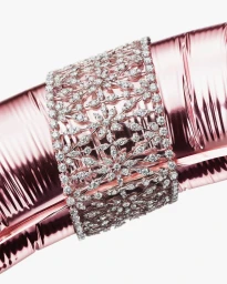Close-up of a wide diamond cuff bracelet worn on a shiny pink metallic cylindrical surface against white
