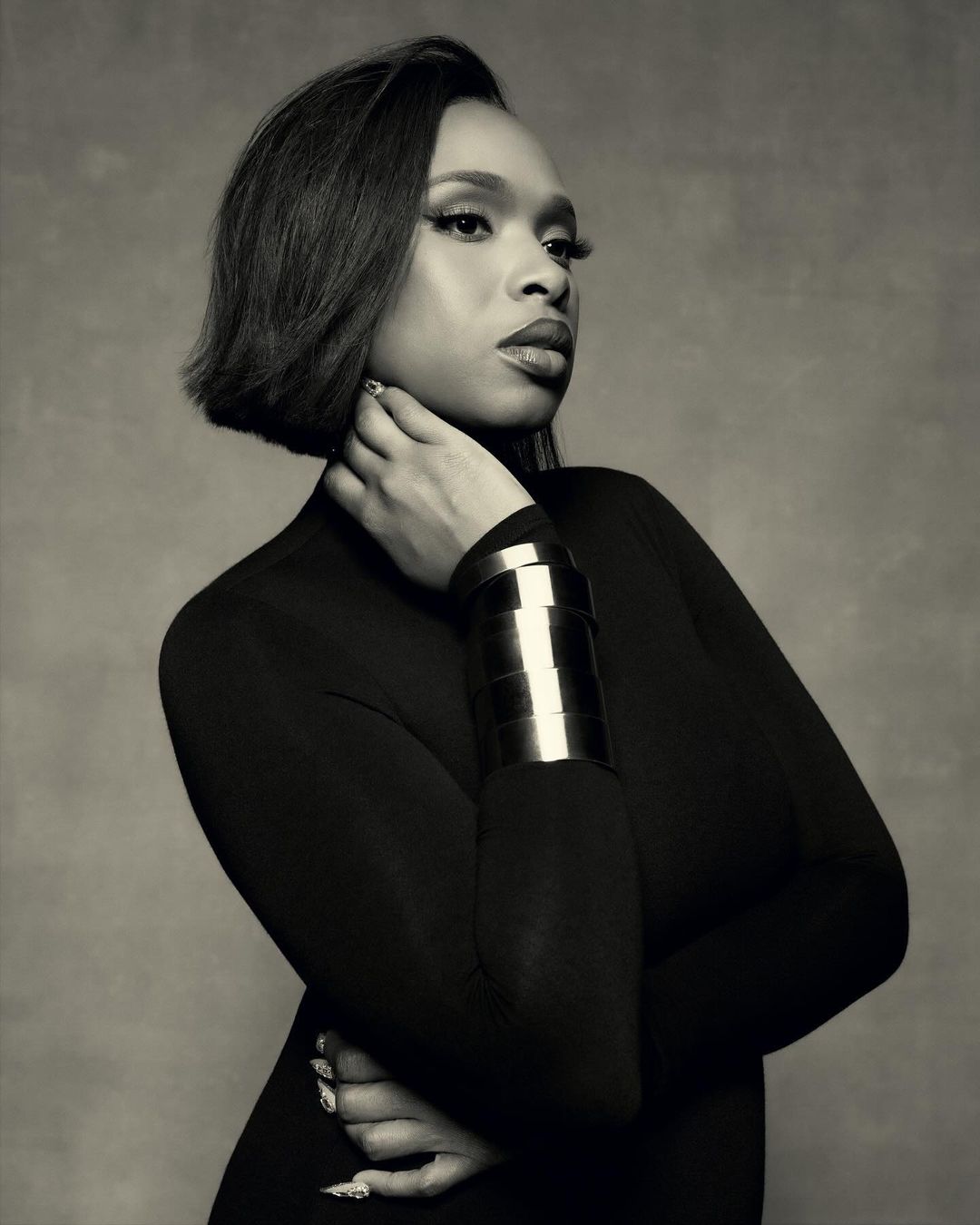 Monochrome portrait of adult woman with bob haircut and metal cuff bracelet against a textured background in a studio setting.