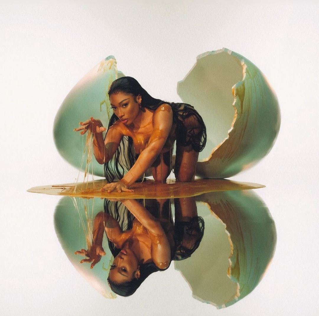 Woman poses in an eggshell with honey. The scene is mirrored in a pool of honey. This surreal image has beauty and fashion appeal.
