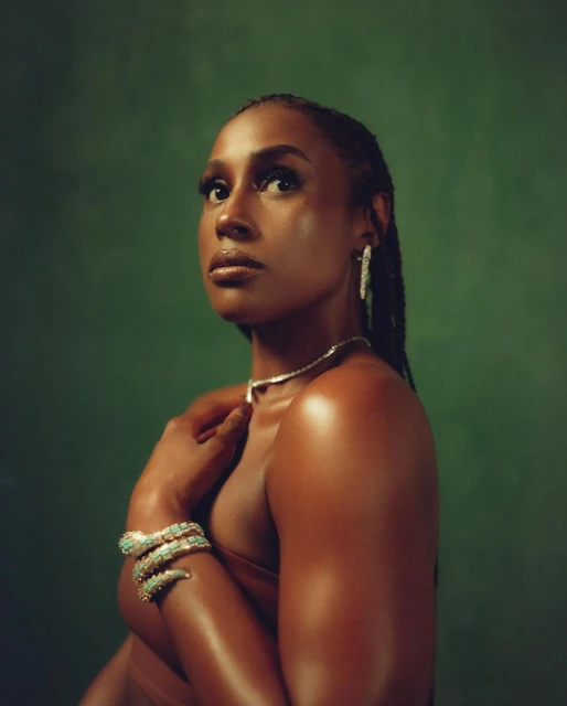 Portrait of a black woman with braided hair wearing statement jewelry against a solid green backdrop in a photo studio setting.