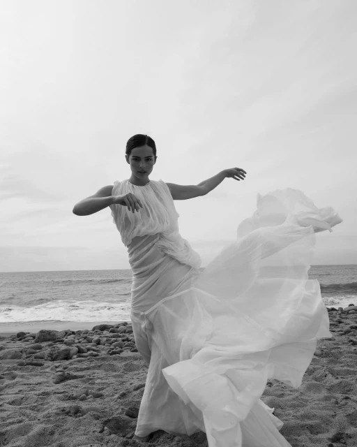 Woman in flowing white dress on beach. An adult female is walking in a white dress with a relaxed facial expression and a beach background.