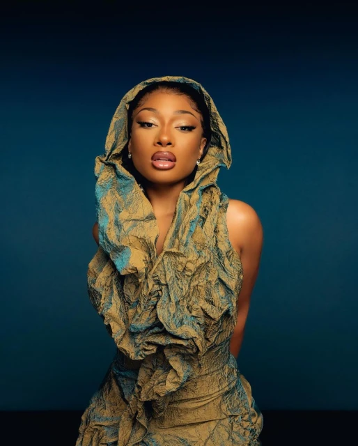 Portrait of an African-American woman wearing an olive and turquoise dress and hooded cape against a deep blue background.