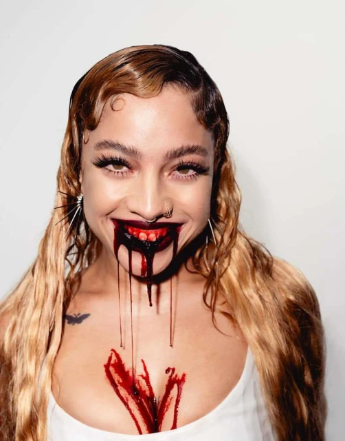 Smiling woman with vintage hairstyle, a nose ring, and red liquid dripping from her mouth and chest against a white background.