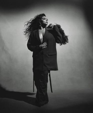 Black and white portrait of a woman with long wavy hair wearing an oversized blazer and holding a feather piece by Kanya Iwana.