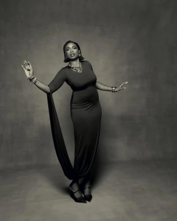 Monochrome portrait of a woman in a long fitted dress with statement jewelry against a textured backdrop