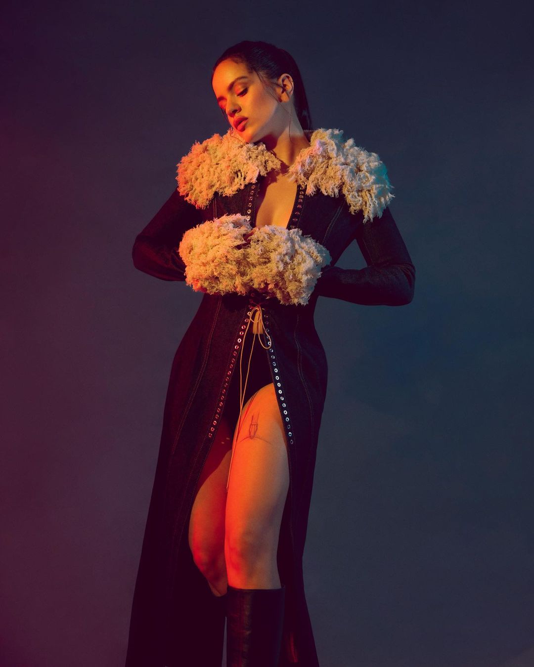 Rosalia wearing a black slit dress with fluffy white fur collar and cuffs under dramatic red and blue studio lighting.
