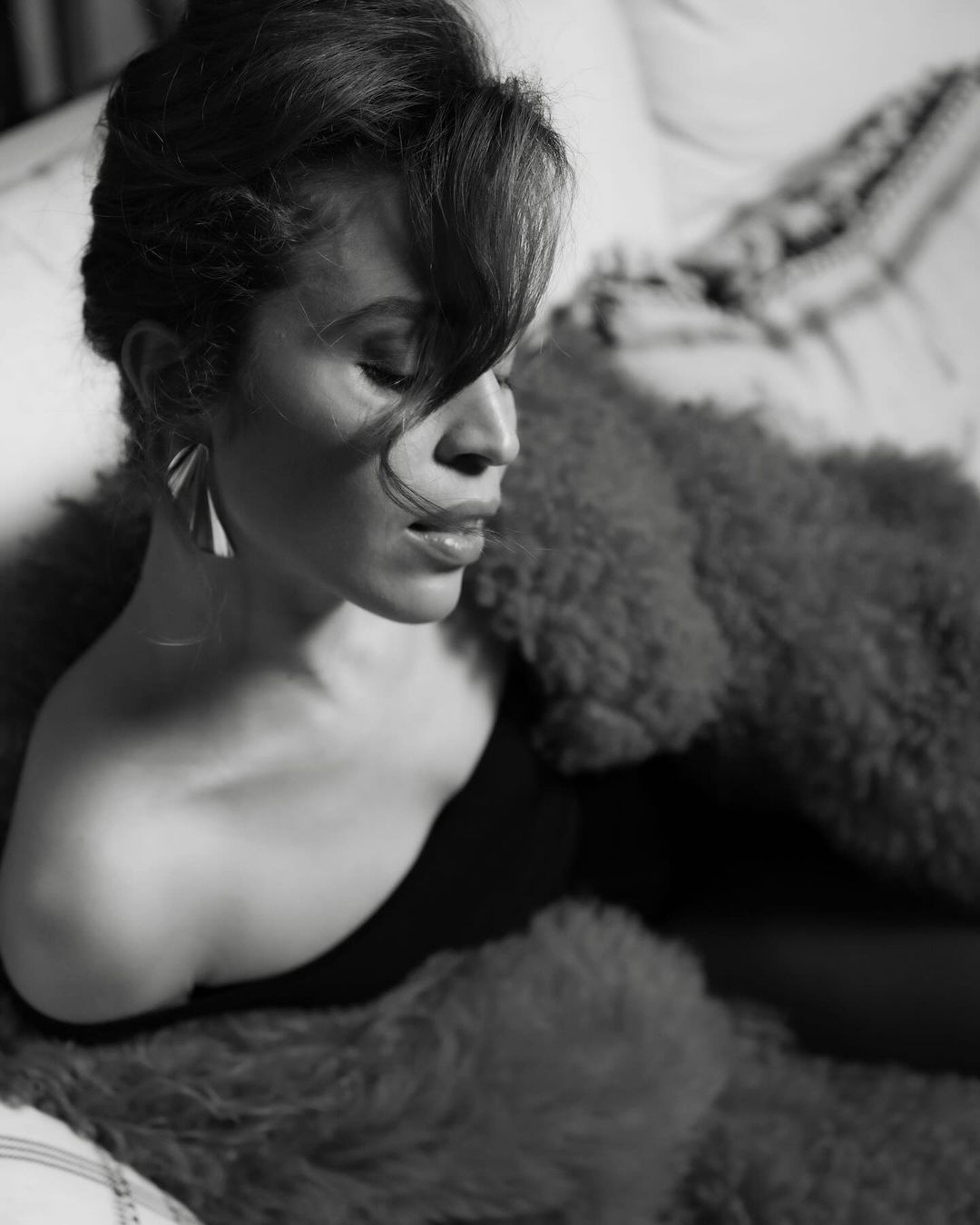 Black-and-white portrait of a woman with an off-the-shoulder top and statement earrings, posing with a fur throw.