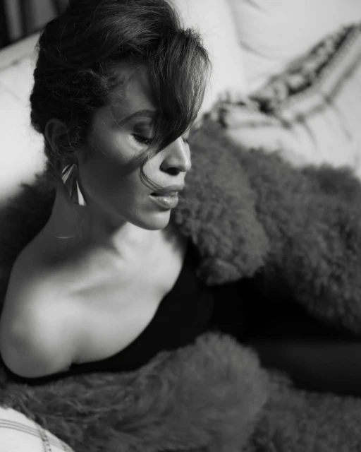 Black-and-white portrait of a woman with an off-the-shoulder top and statement earrings, posing with a fur throw.