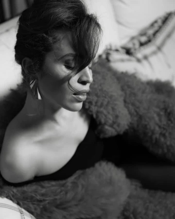 Black-and-white portrait of a woman with an off-the-shoulder top and statement earrings, posing with a fur throw.
