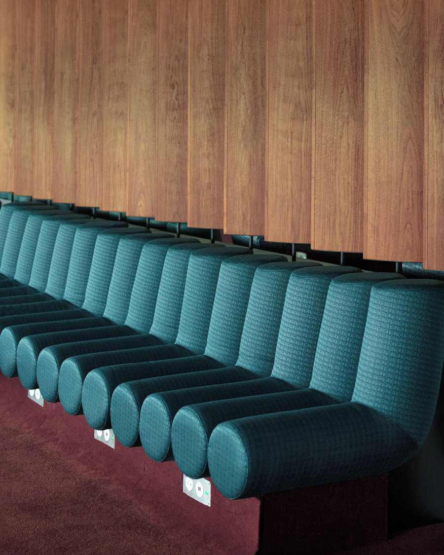 Interior view of teal textured seating, and a wood-paneled wall, creating a modern, architectural space with warm and cool tones.