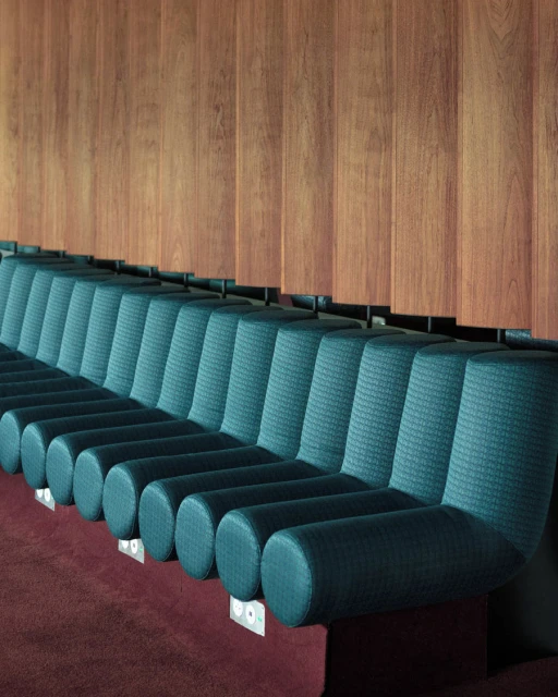 Interior view of teal textured seating, and a wood-paneled wall, creating a modern, architectural space with warm and cool tones.
