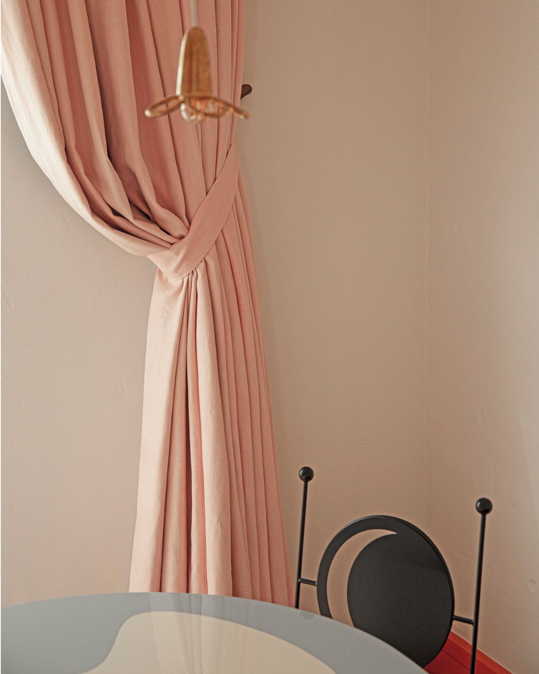 Interior design shot featuring a pink curtain, a hanging lamp, and a black chair with a light grey and white table underneath it.