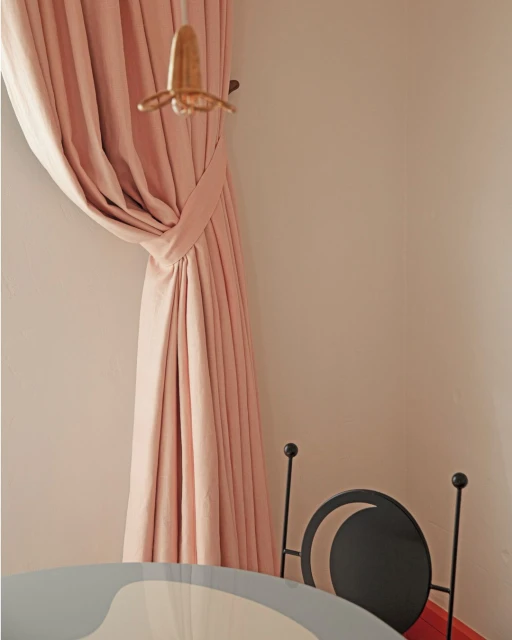Interior design shot featuring a pink curtain, a hanging lamp, and a black chair with a light grey and white table underneath it.