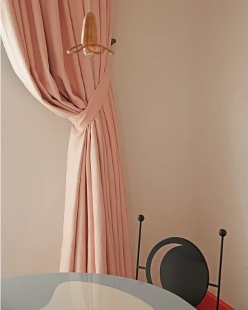 Interior design shot featuring a pink curtain, a hanging lamp, and a black chair with a light grey and white table underneath it.